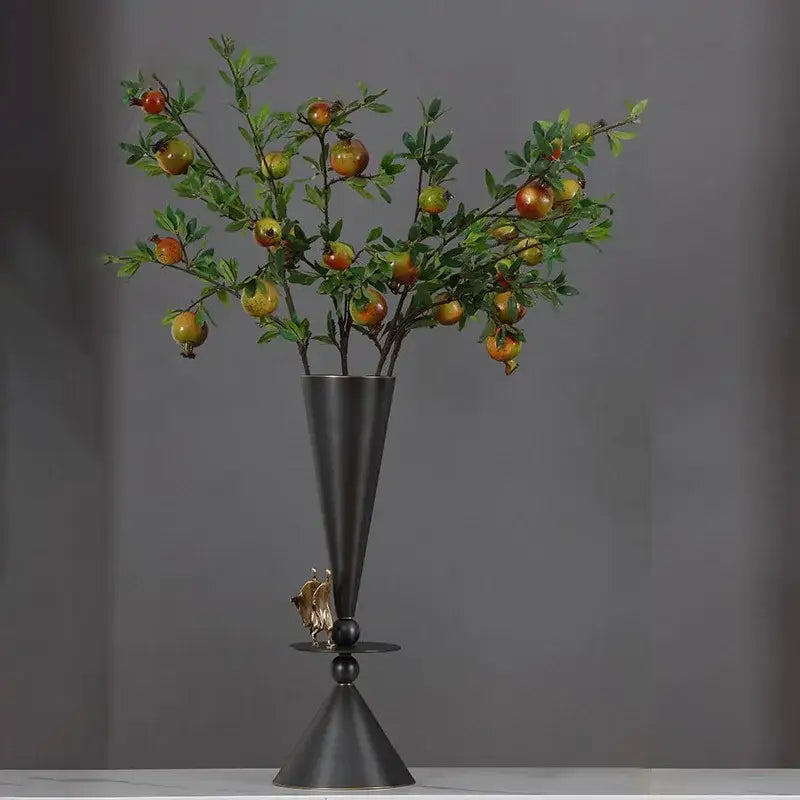 A decorbites bronze flower vase in matte black with gold figurine holds artificial pomegranate branch for dining room decor