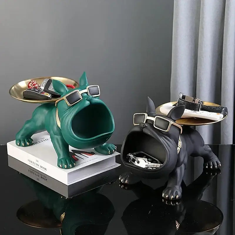 Two stylized teal and black french bulldog figurines with gold framed sunglasses and metallic trays for remote control storage