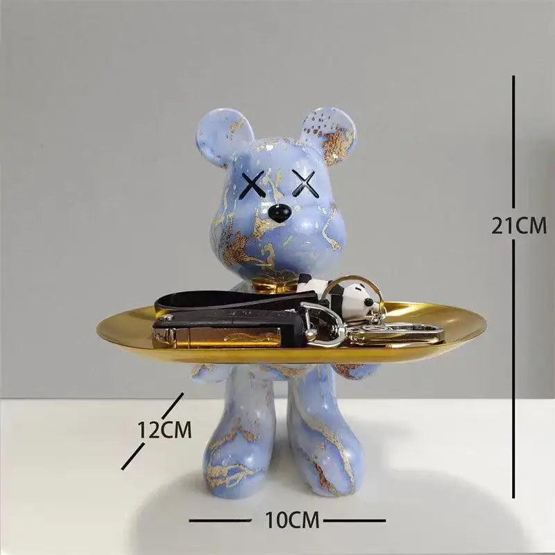A light blue bear figurine with gold leaf accents and x-shaped eyes holding a golden tray decorbites graffiti bear decor