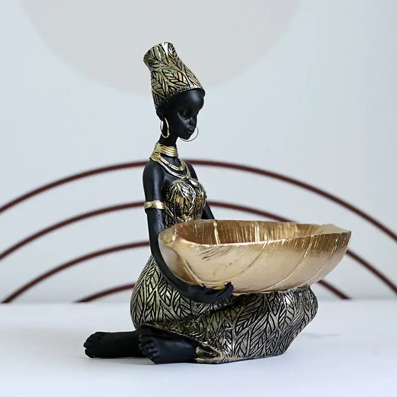 Black and gold resin black woman figurine seated holding a golden bowl with intricate leaf patterns for living room decor