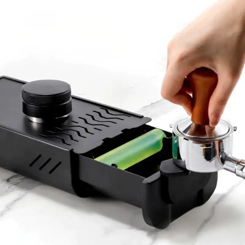 Black espresso machine with green coffee tamper and chrome portafilter on black and green barista tamping station tray
