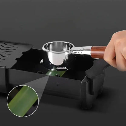 Black and green barista tamping station tray with a black plastic knockbox grounds bin and stainless steel espresso maker