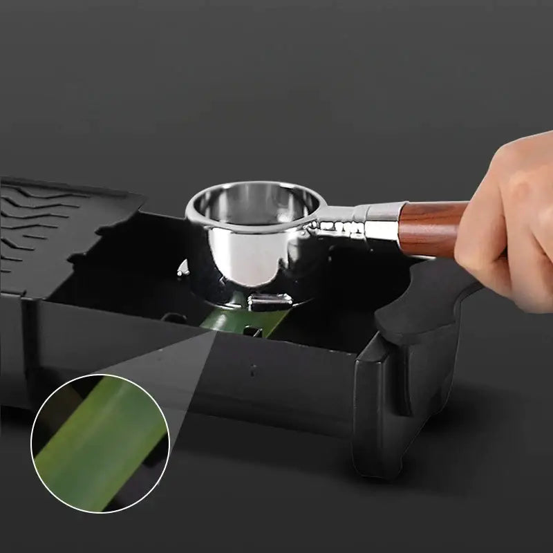 Black and green barista tamping station tray with a black plastic knockbox grounds bin and stainless steel espresso maker