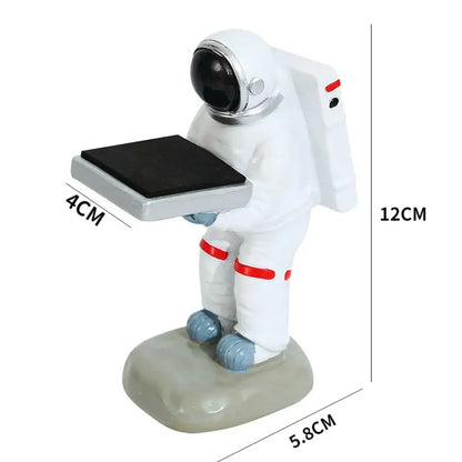 White astronaut figurine with red accents and silver helmet holding black solar panel on cartoon bear watch stand