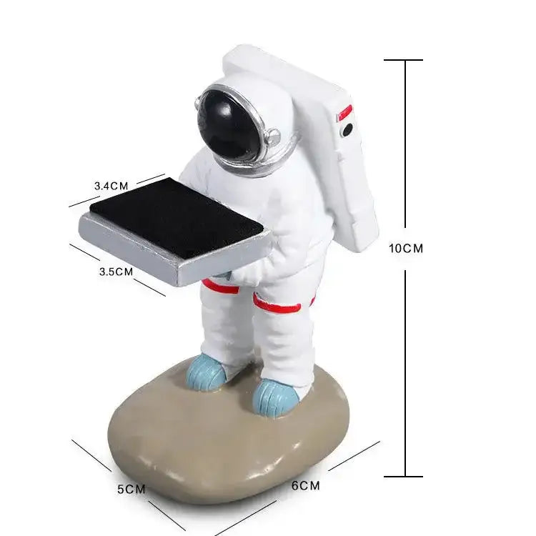 White astronaut figurine with blue boots holding silver-framed tablet on black and iridescent purple cartoon bear watch stand