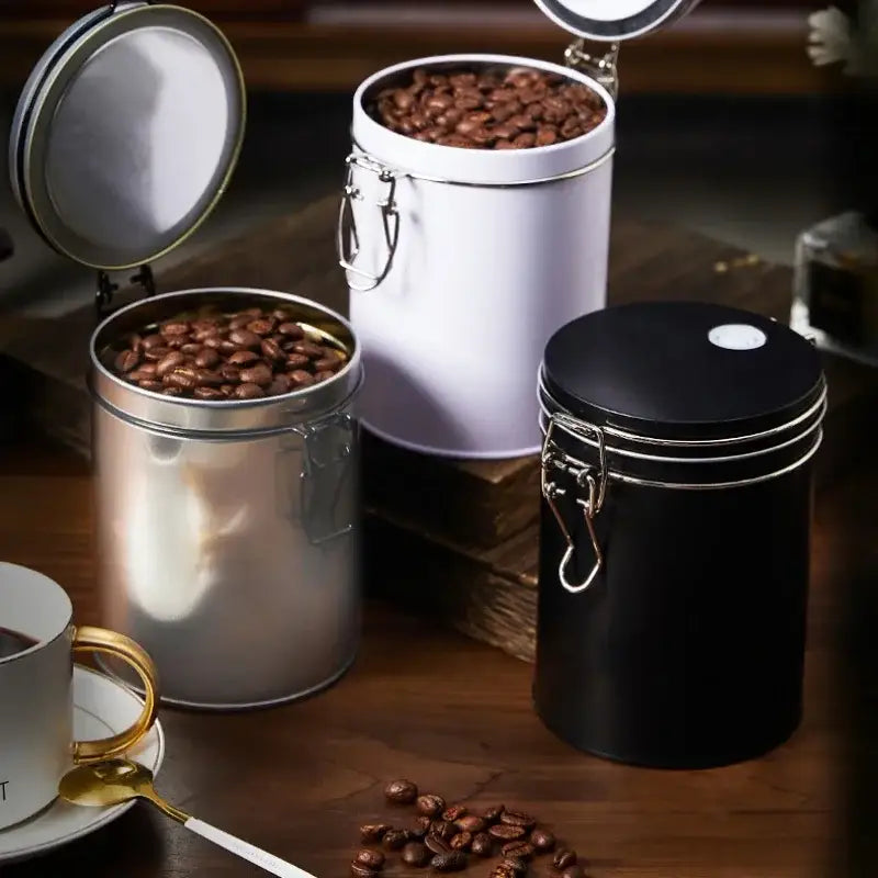 Three cylindrical metal food storage pots in silver black and white with clamp lids by decorbites hermetic food storage