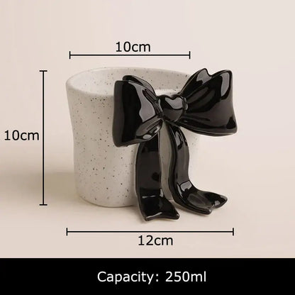 A porcelain coffee cup featuring a speckled white ceramic body with a sleek black glossy bowknot accent on the side