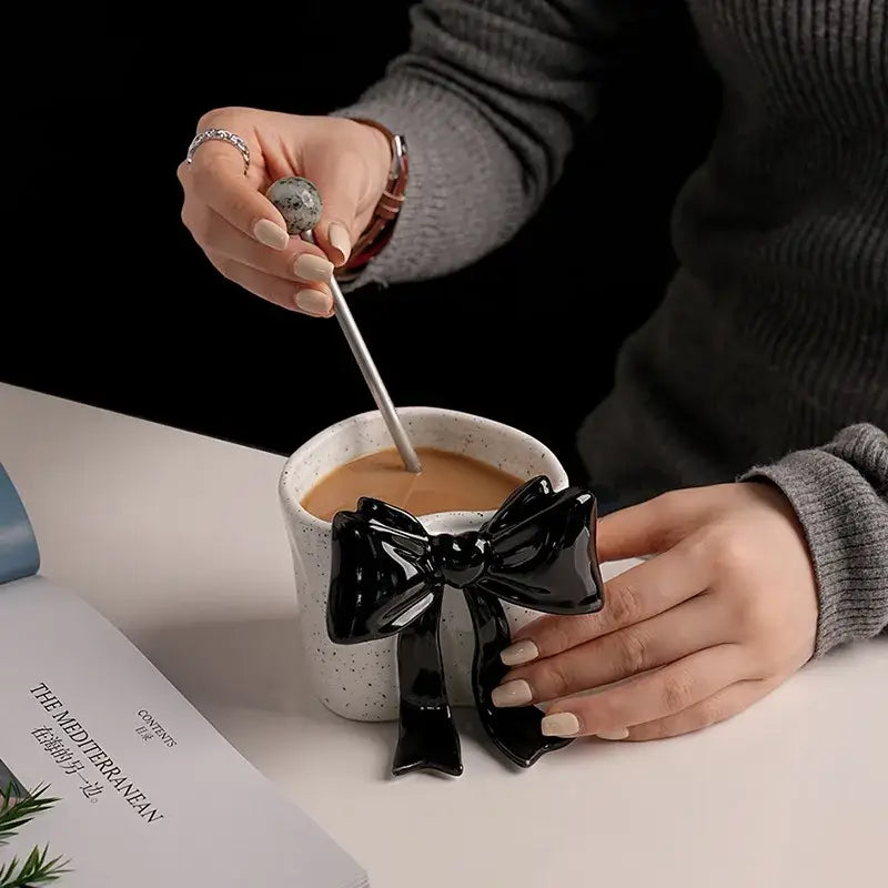 A white speckled porcelain coffee cup with a glossy black bow-shaped handle for dining room use