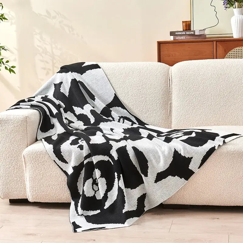 Black and white camellia knitted blanket with bold rose pattern draped over beige sofa by decorbites camellia
