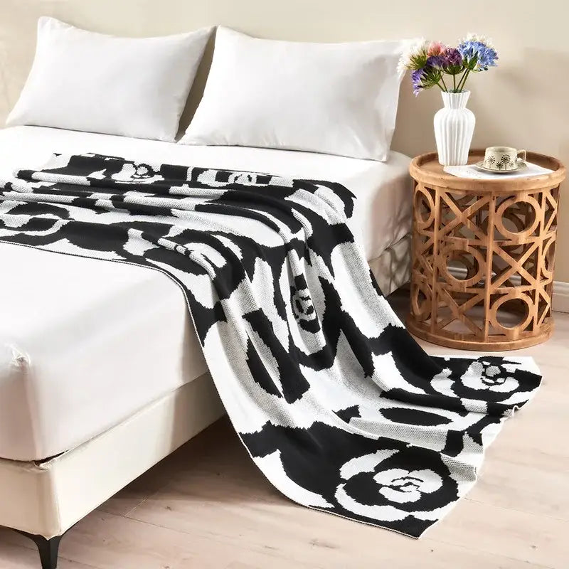 Black and white camellia knitted blanket with bold floral pattern draped over bed by decorbites camellia knitted