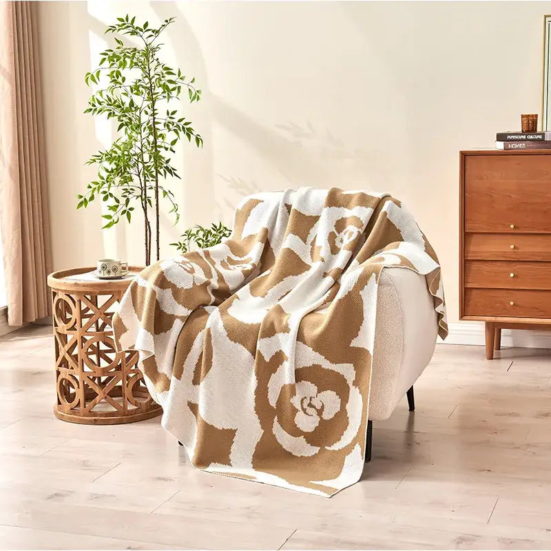 A cozy cream and tan floral camellia knitted blanket draped over a chair from decorbites camellia collection
