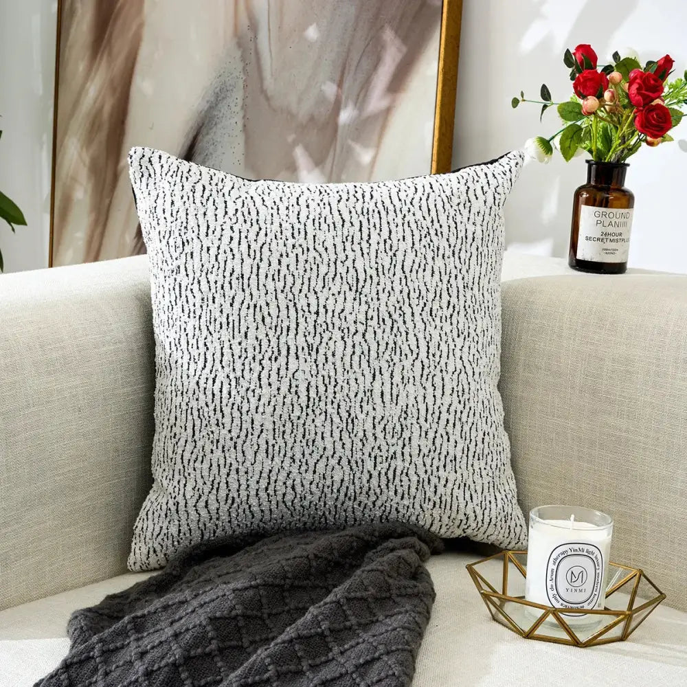 A black and white geometric chenille pillow cover with subtle textured pattern on an off-white cushion for living room decor