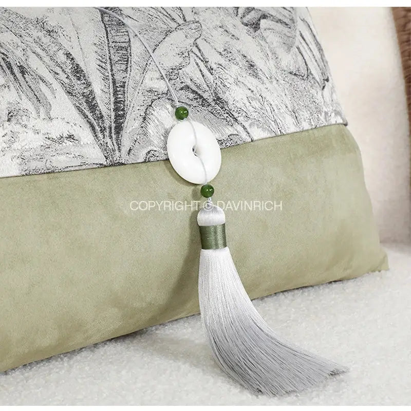 A delicate white tassel with jade-like beads hanging from a black and white green jungle plants pillow cover