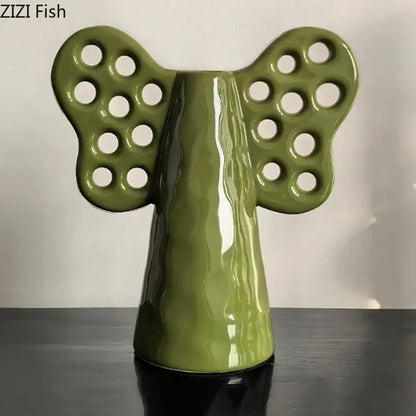 Olive-green ceramic angel figurine with circular cutouts on wings complementing decorbites elephant ceramic vase with artificial flowers