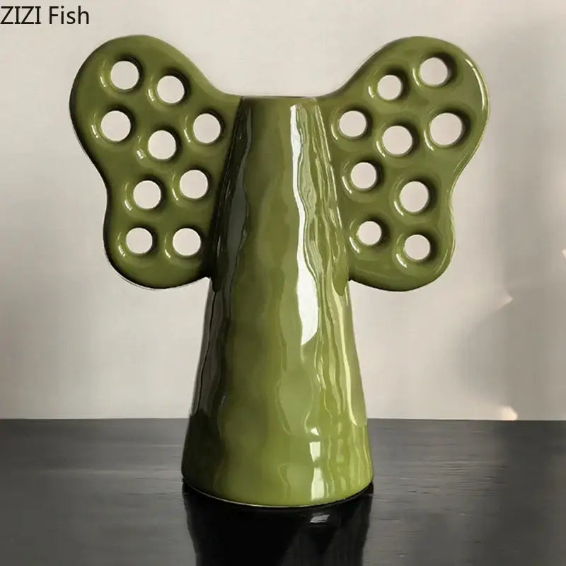 Olive-green ceramic angel figurine with circular cutouts on wings complementing decorbites elephant ceramic vase with artificial flowers