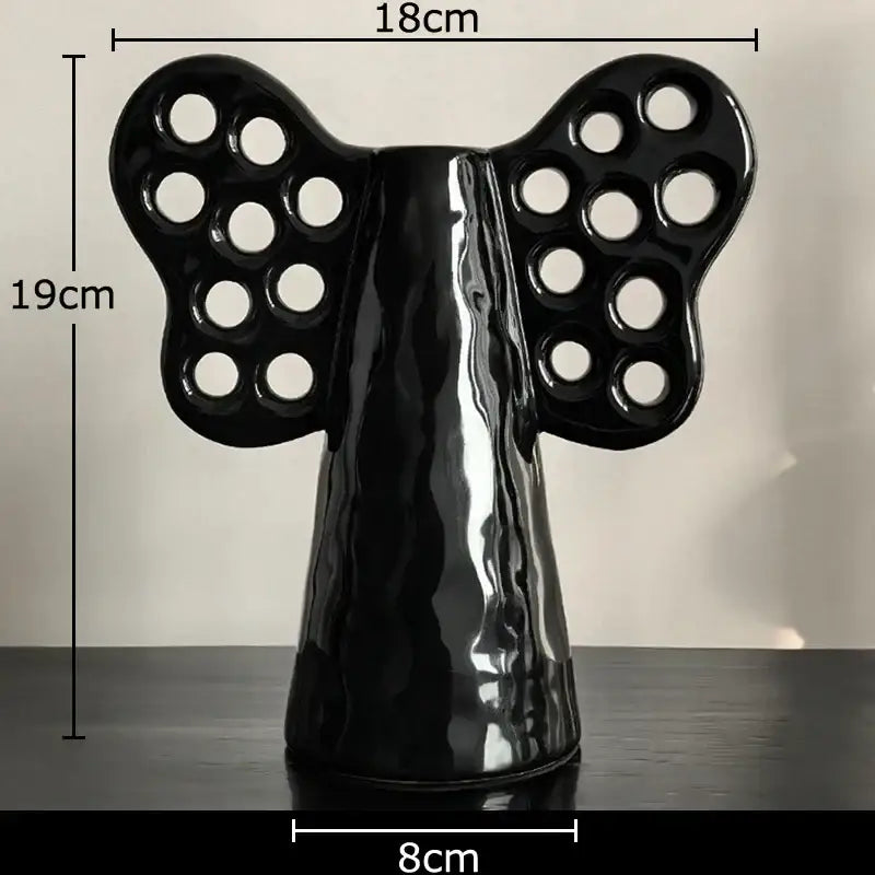 Black glossy ceramic angel figurine with butterfly winged back with circular cutouts in decorbites elephant ceramic vase with artificial flowers for living room decor