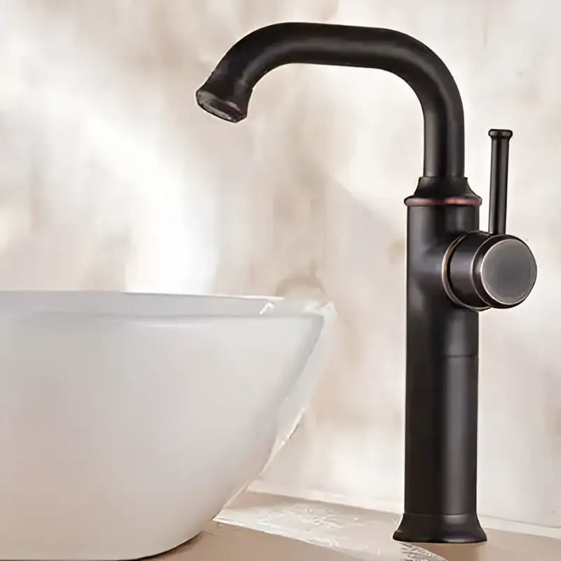 Black antique brass basin faucet with matte black curved spout and cylindrical handle beside white sink by decorbites