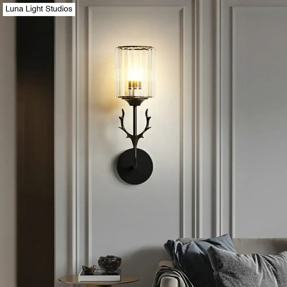 Black metal wall sconce with antler-inspired design and clear glass cylinder housing three warm-toned e26 e27 bulbs