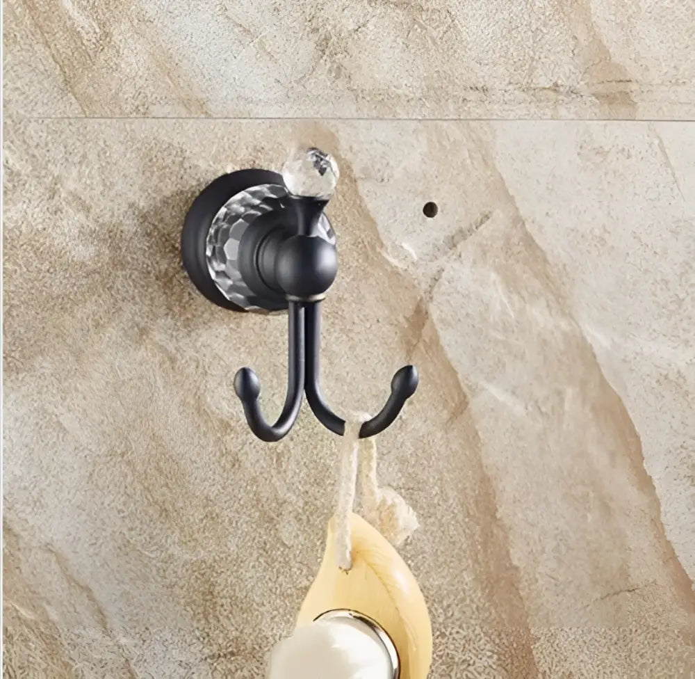 Black brass double hook with faceted crystal accent mounted on stone wall in bathroom accessories set
