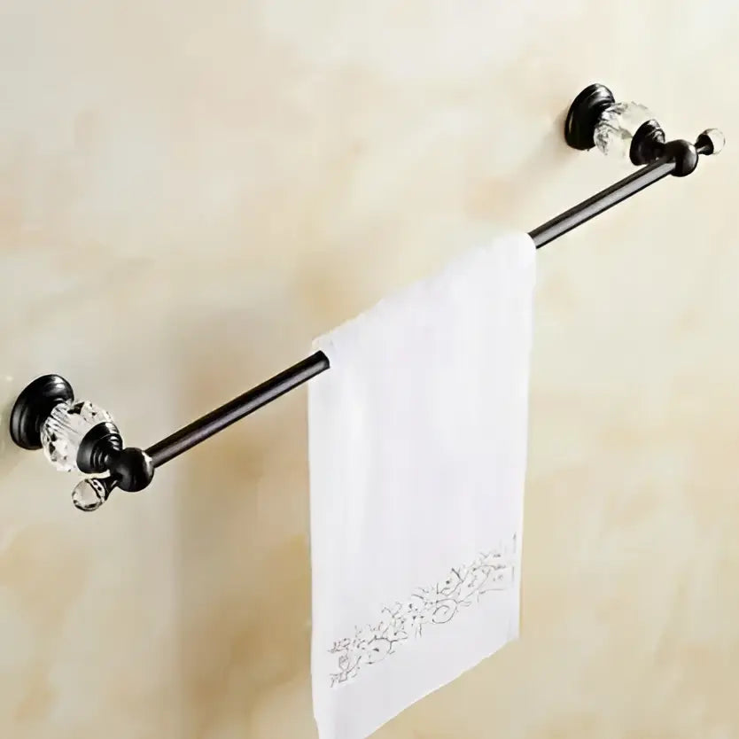 Black brass towel rack with crystal embellishments holding a white embroidered towel in bathroom accessories set