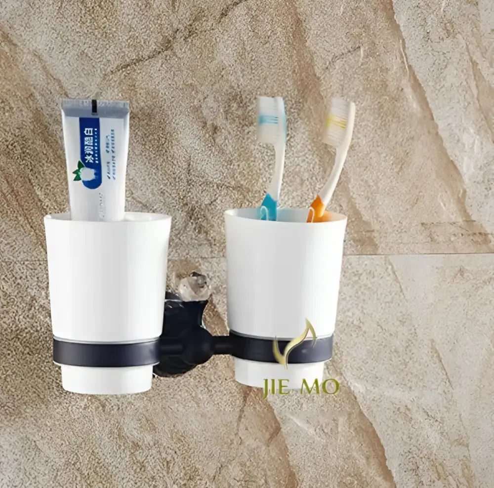 White ceramic toothbrush holder with black accent band and two cups in black brass bathroom accessories set mounted on wall bracket