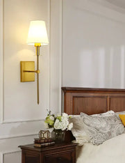 Gold-toned black brass wall sconce with tapered fabric shade for bedroom lighting