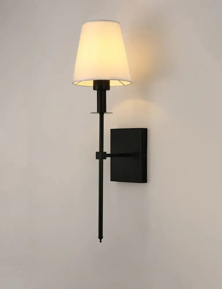 Black brass wall sconce with a cream fabric shade designed for bedroom lighting and decorative use