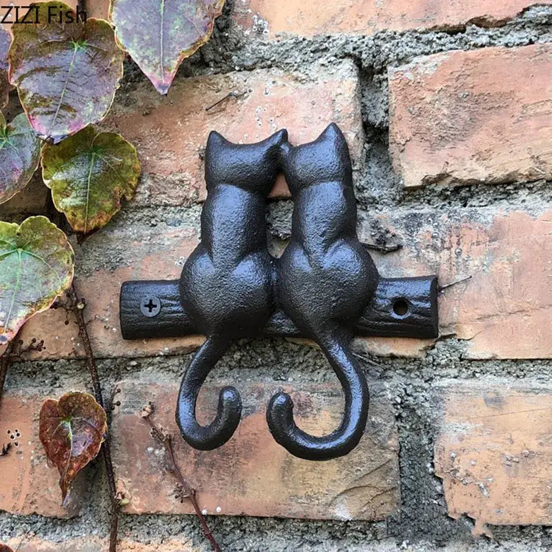 Black cast iron cat hook shaped like two cats facing each other mounted on a brick wall for hanging shelf decorbites cat hook