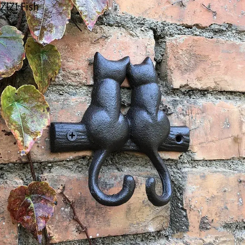 Black cast iron decorbites cat hook shaped like two cats sitting back-to-back on a wooden branch for hanging shelf decor