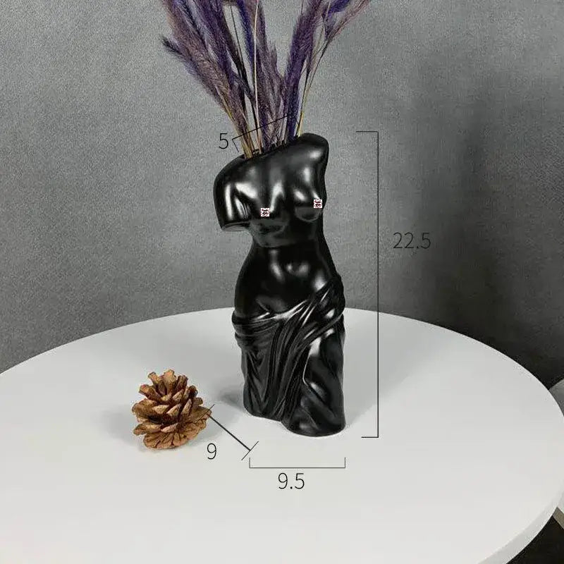 Black glossy ceramic human body figurine bust vase shaped like female torso with draped fabric holding purple dried grass