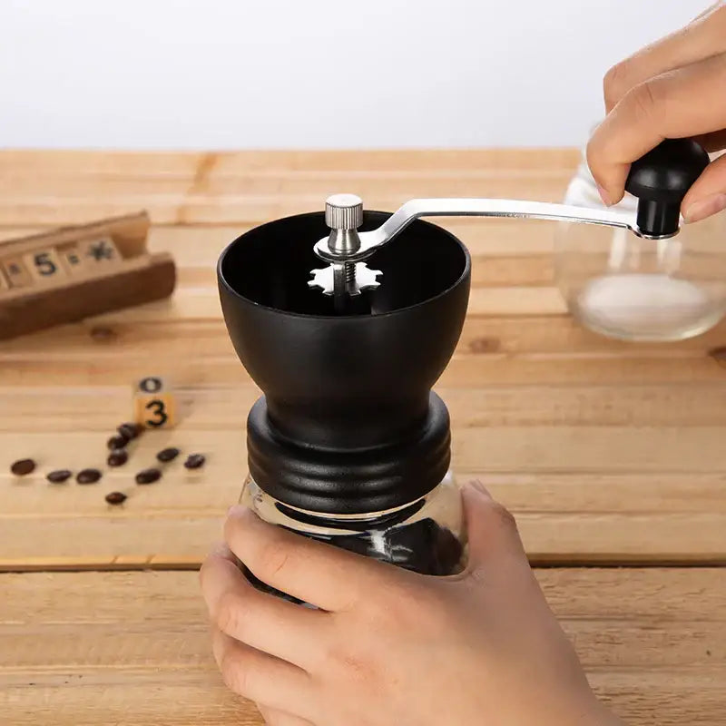 Black ceramic hand rocking coffee grinder with clear glass container and silver metal handle for manual kitchen use