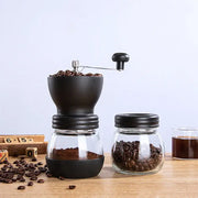 Black ceramic hand rocking coffee grinder with glass base and metal crank handle for manual kitchen milling