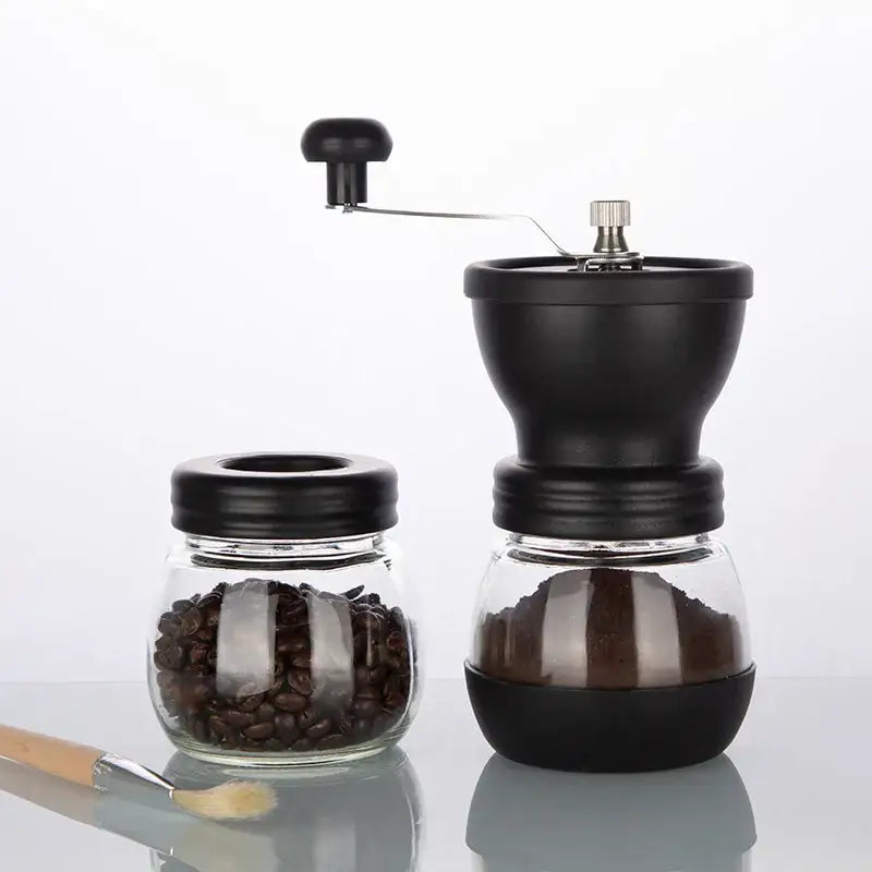 Black ceramic hand rocking coffee grinder with metal crank handle and glass base filled with ground coffee for kitchen use