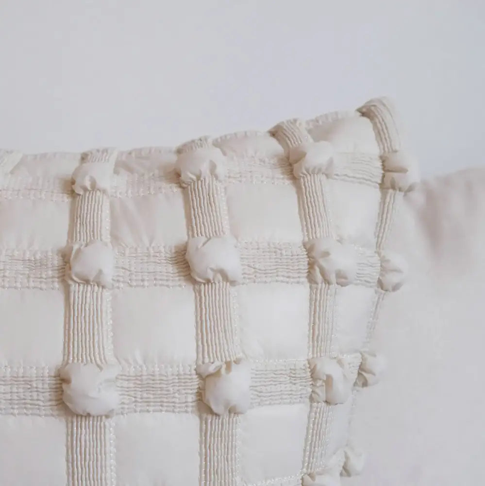 Off-white quilted cushion cover with dot bubble textured grid and pom pom detailing for home decor