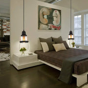 Black industrial cylinder pendant lighting with clear glass shades and exposed bulbs hangs above a white nightstand in living room
