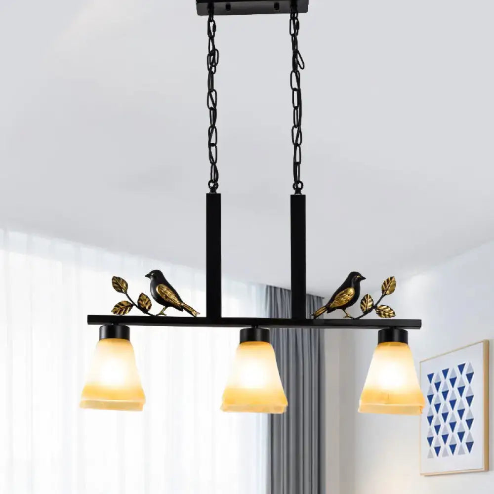 Decorbites black metal light pendant with ornate bird and leaf details and three warm tan glass shades for dining room island