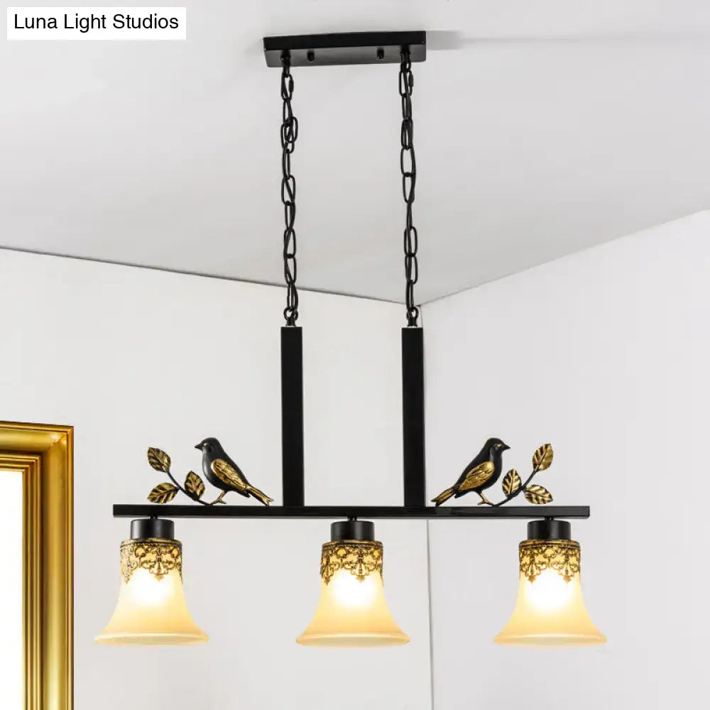 DecorBites black metal light pendant with gold bird and leaf details and three tan glass shades for dining room island