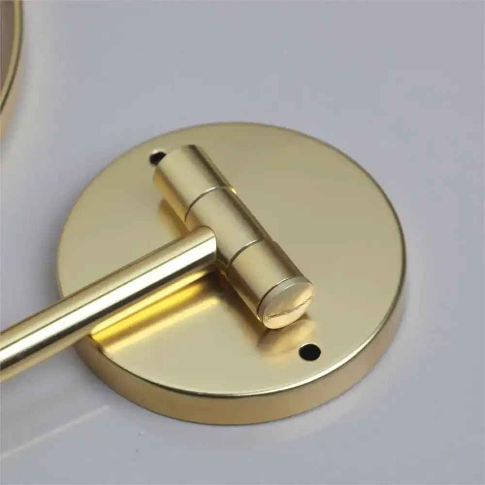Gold-finished metal wall mounted towel rack with circular base and articulated arm complementing decorbites 3x magnifying mirror