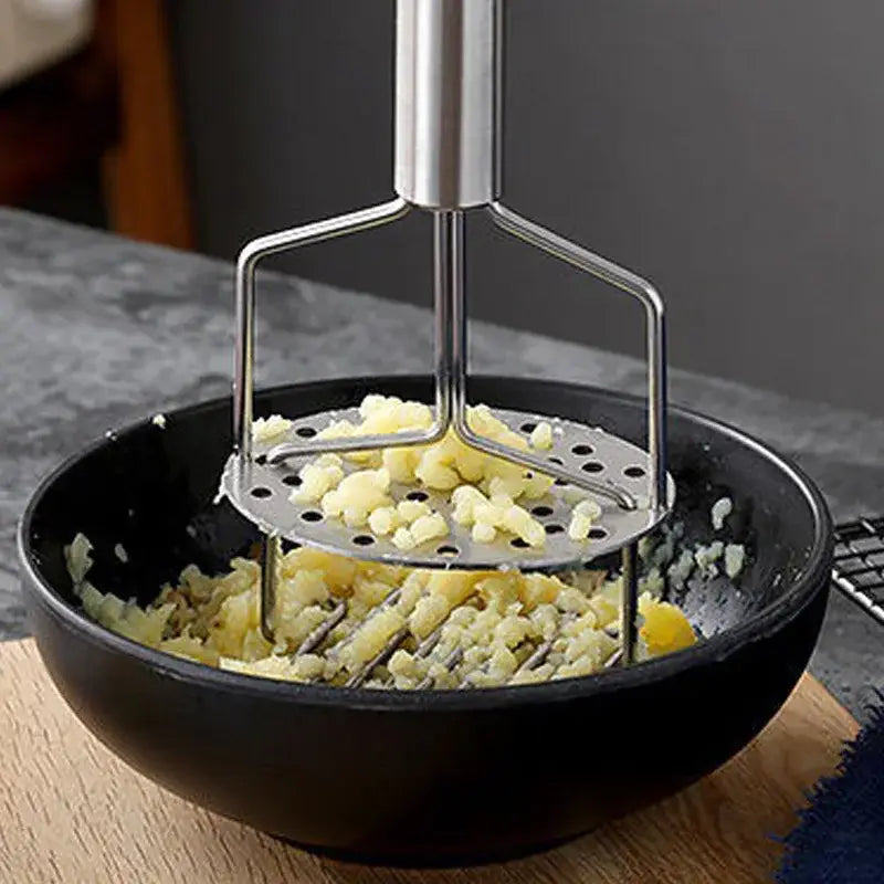 Black and silver stainless steel potato masher with perforated head and sturdy handle in black bowl of mashed potatoes
