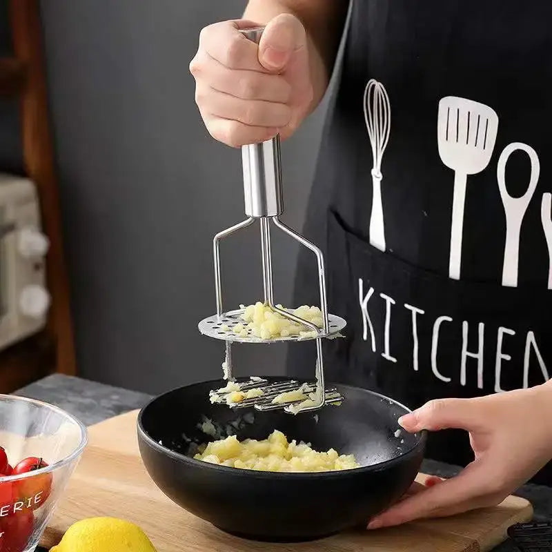 Black and silver stainless steel potato masher with handle and perforated base mashing potatoes in a black bowl