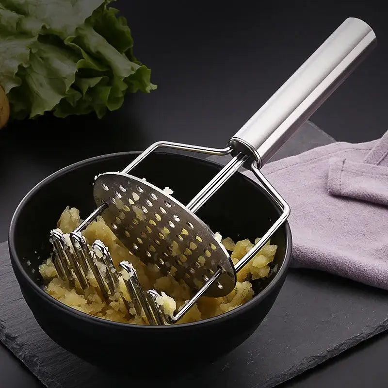 Black and silver stainless steel potato masher with long handle and perforated head resting in mashed potatoes bowl