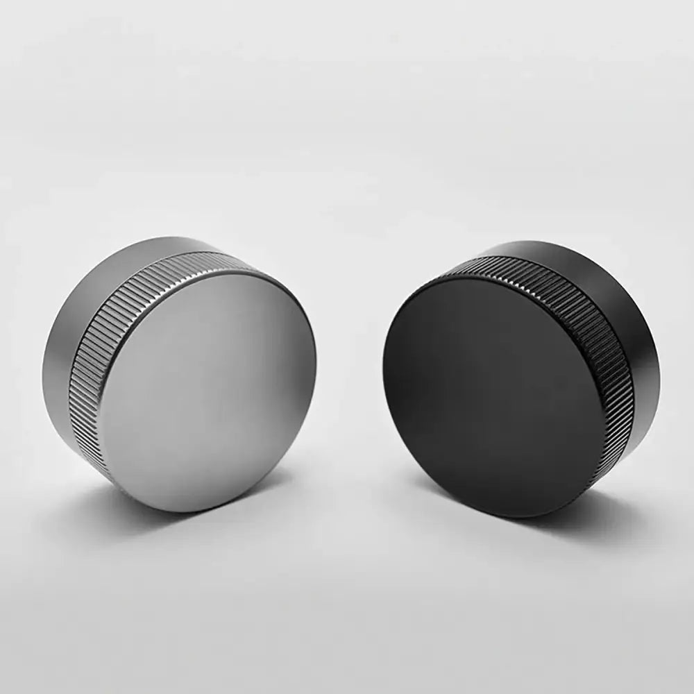 Two cylindrical metal decorbites espresso tamper caps with textured ridged edges in matte silver and glossy black finish