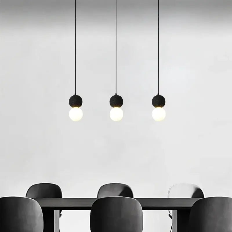 Three minimalist black travertine led pendant lights with spherical glass bulbs hang above a dining table decorbites black travertine