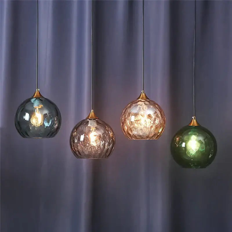 Four hanging glass ball pendant lights with textured frosted surfaces in blue amber rose gold and green by decorbites