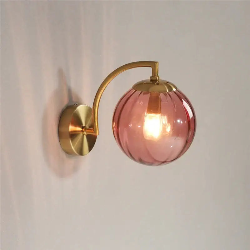 A blush pink ribbed colored glass ball wall lamp with brass finish metal arm for bedroom decorbites lighting