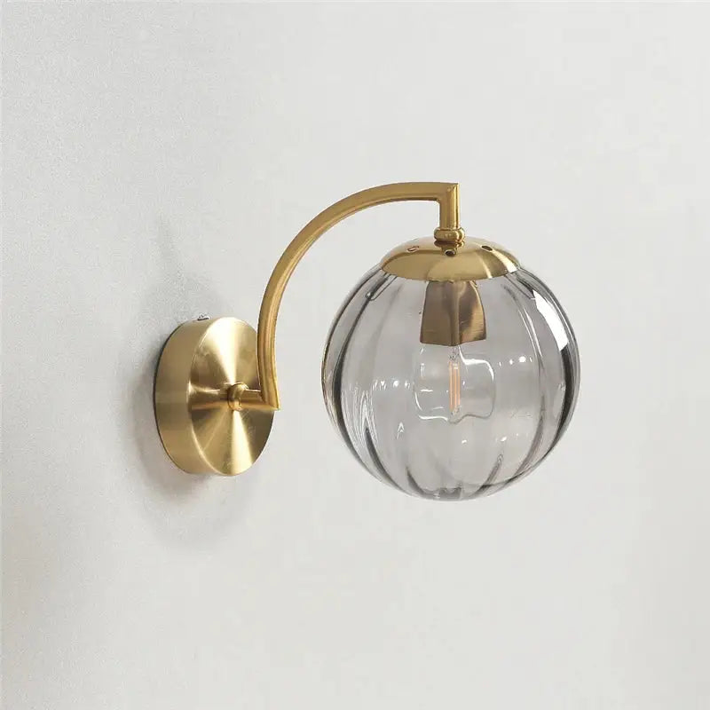 A sleek brass-finished wall lamp with a blue and brass colored glass ball for bedroom lighting decorbites colored glass