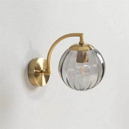 A sleek brass-finished wall lamp with a blue and brass colored glass ball for bedroom lighting decorbites colored glass