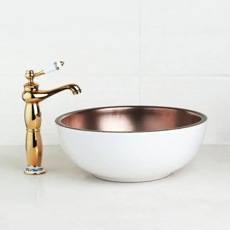 White ceramic painted ceramic vessel sink set with copper interior and gold-toned faucet with porcelain handle