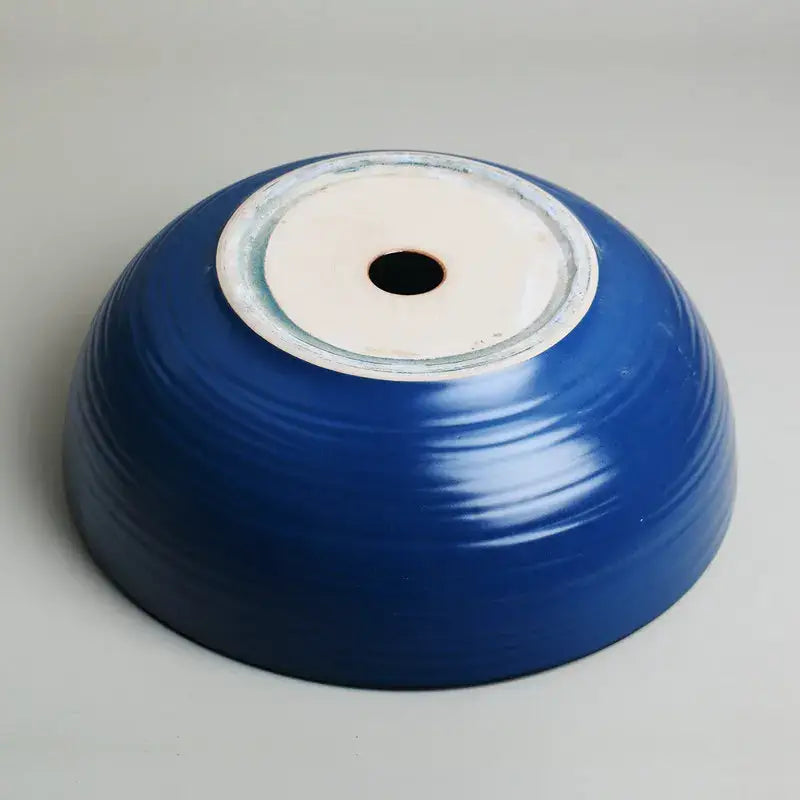A glossy cobalt blue hand painted ceramic vessel sink set with concentric ridges and a white circular base hole