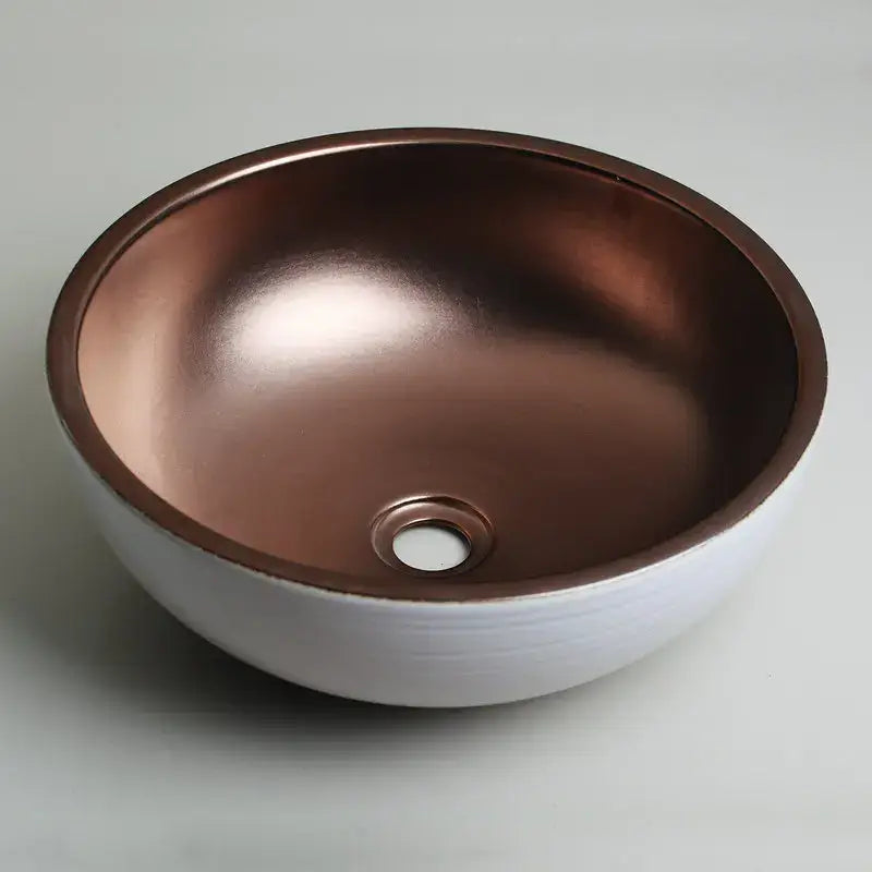 A hand painted ceramic vessel sink set with a white exterior and polished copper interior for bathroom use